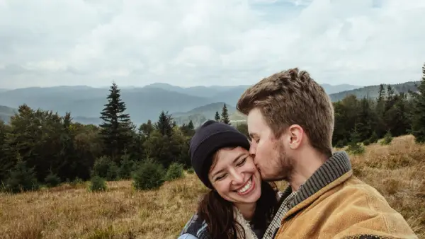 A couple kissing with an open field and mountains in the background